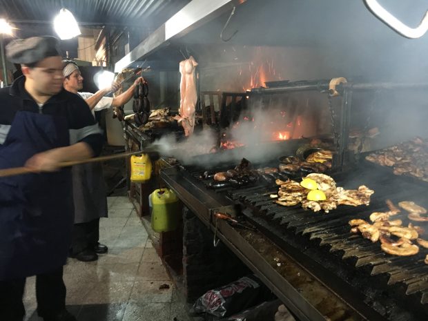 Guys cooking steaks, chicken on Argentine parrilla